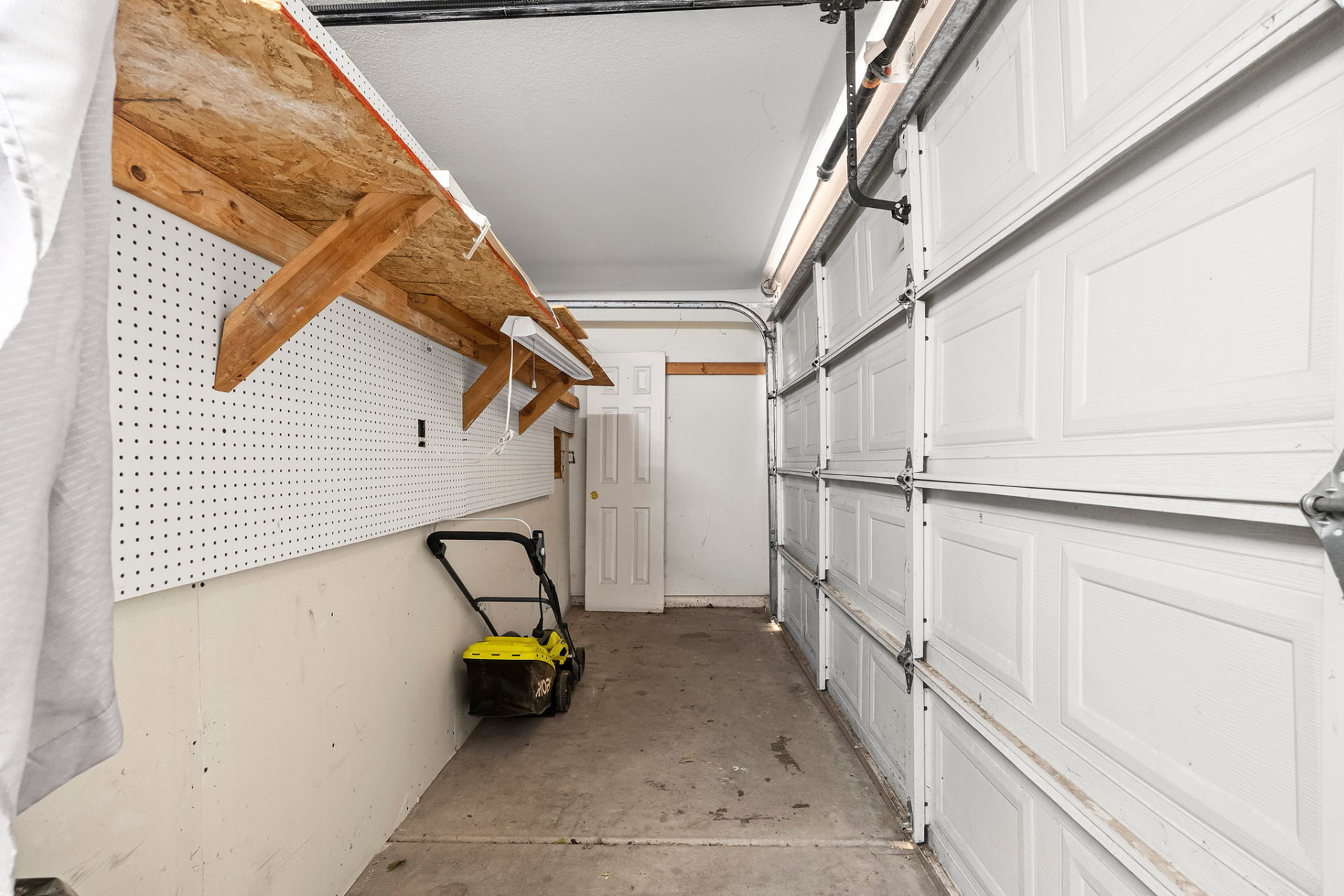Garage storage space with pegboard wall and overhead shelving, room for a workbench